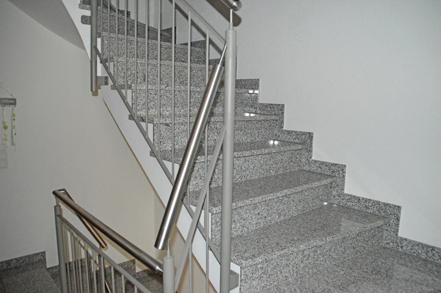 Moderne Innentreppe mit grauem Granit und silbernem Edelstahlgeländer in hellem Treppenhaus