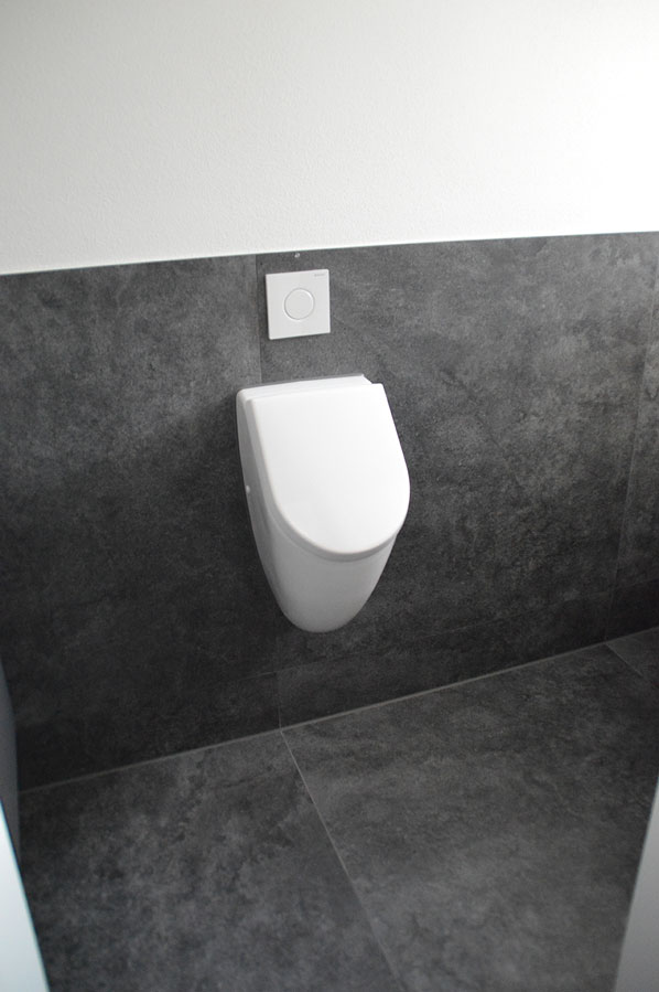 Modernes Urinal an dunkelgrauer Fliesenwand mit Unterputzspülung