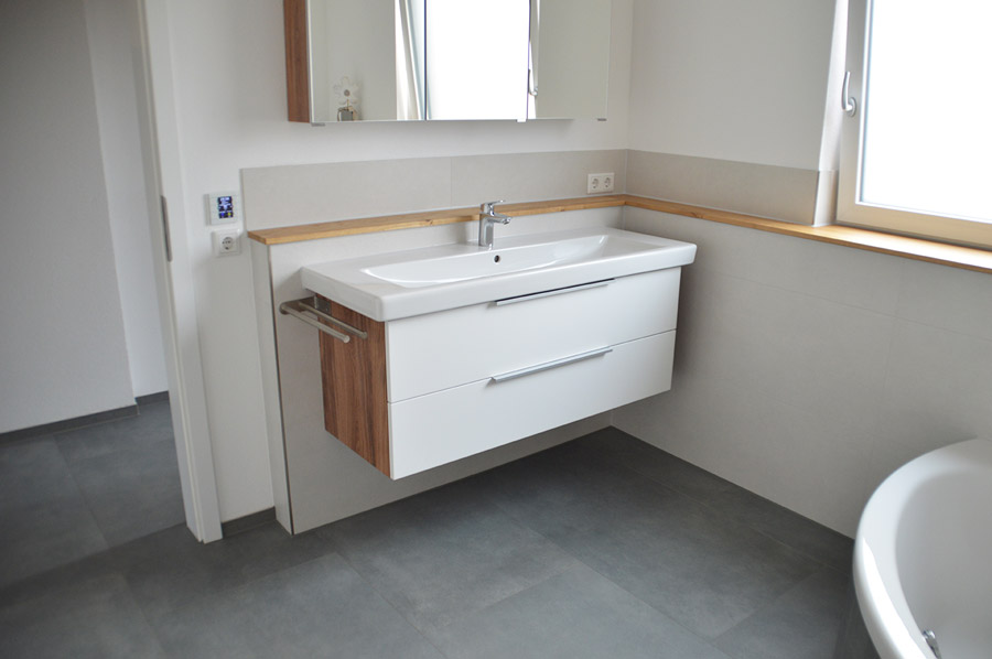 Wandhängender Waschtisch in Weiß mit Holzakzenten auf grauem Fliesenboden