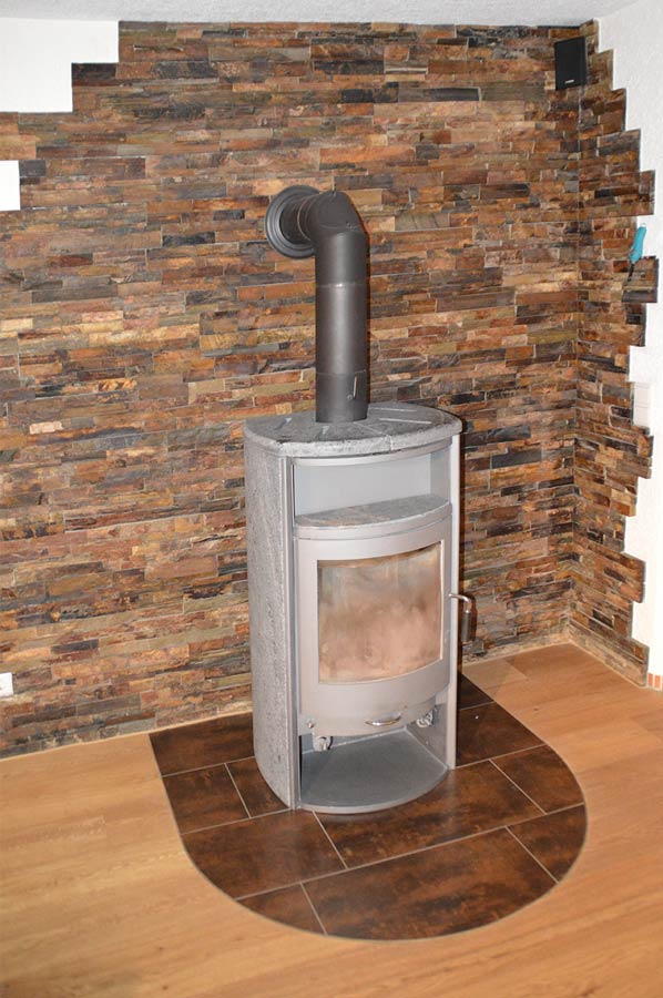 Moderner Schwedenofen vor dekorativer Natursteinwand in Braun- und Rottönen mit Fliesenschutz