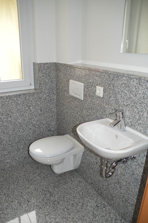 Kompaktes WC mit wandhängendem Waschbecken und grauer Granit-Wandverkleidung