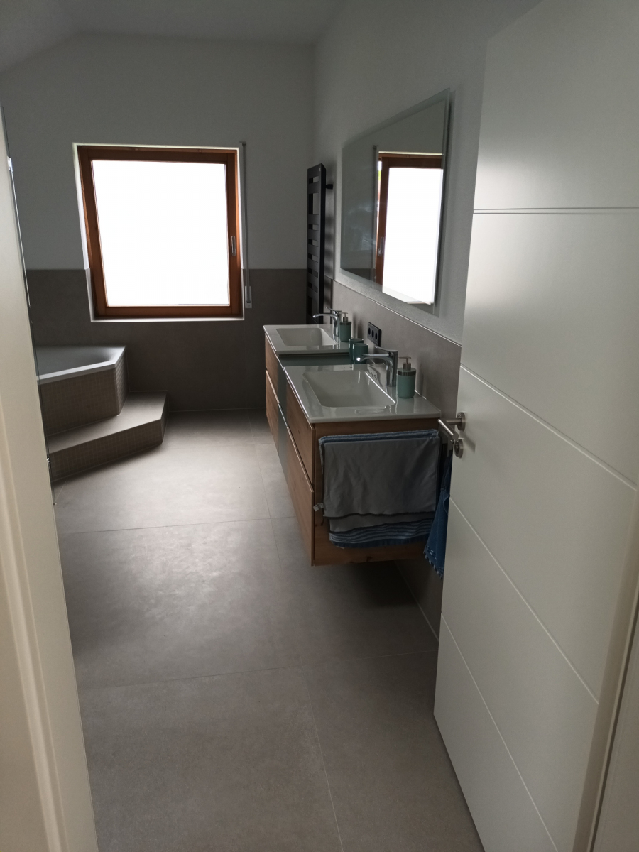 Langes Bad mit großformatigen grauen Bodenfliesen, Doppelwaschtisch in Holzoptik und Badsitzbank