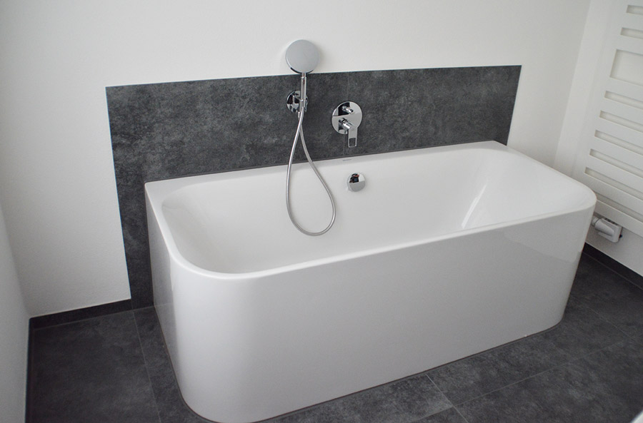 Moderne weiße freistehende Wanne vor anthrazitfarbener Akzentwand mit Unterputzarmatur