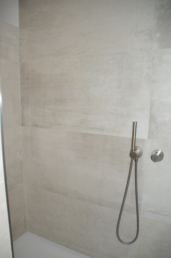 Ebenerdige Dusche mit beigen Großformatfliesen und Unterputzarmaturen in Edelstahl