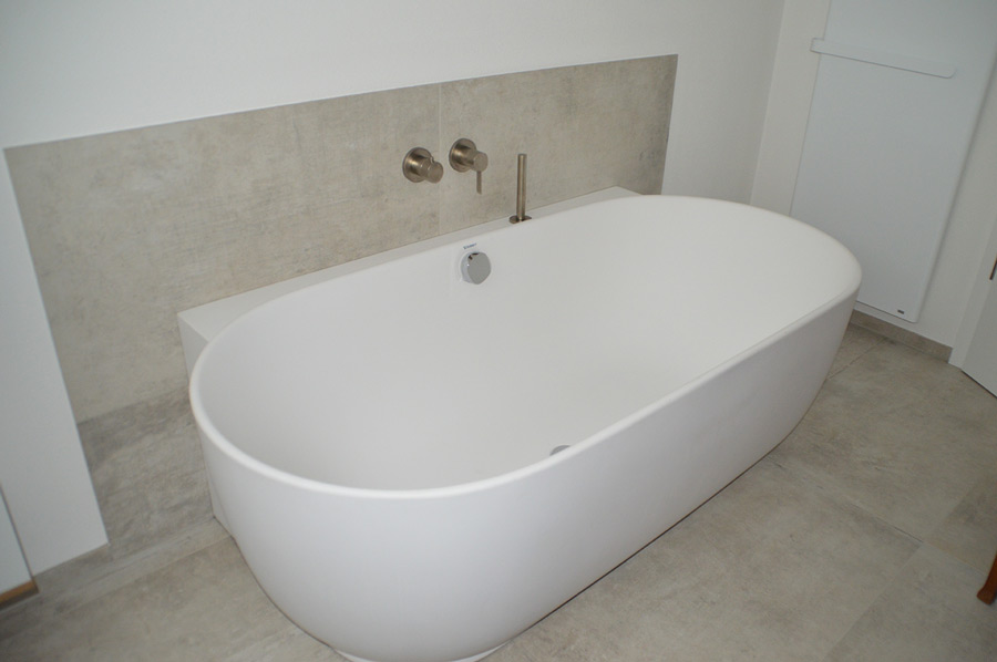 Ovale freistehende Badewanne mit Wandarmatur und heller Fliesenakzentwand